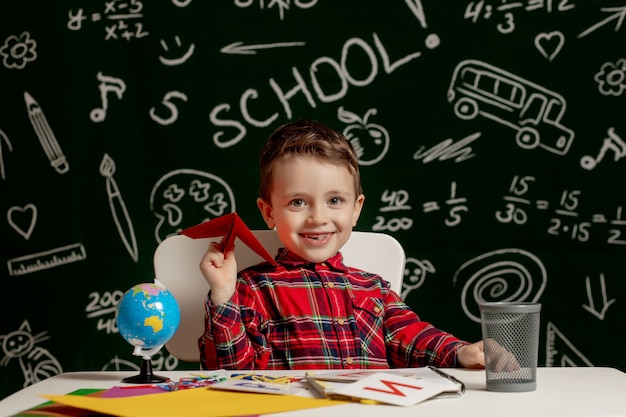 Istruzione a casa o a scuola. Allievo con aeroplano di carta. Ritratto di bambino della scuola elementare.