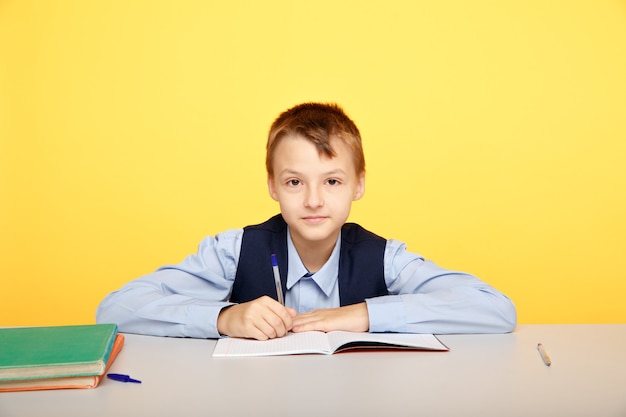 Istruzione al concetto di scuola. Ragazzo seduto al tavolo e studiare isolato nell'aula gialla.