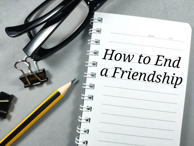 Istruzione conceptText Come terminare un'amicizia su notebook con clip pencilpaper e bicchieri su sfondo grigio