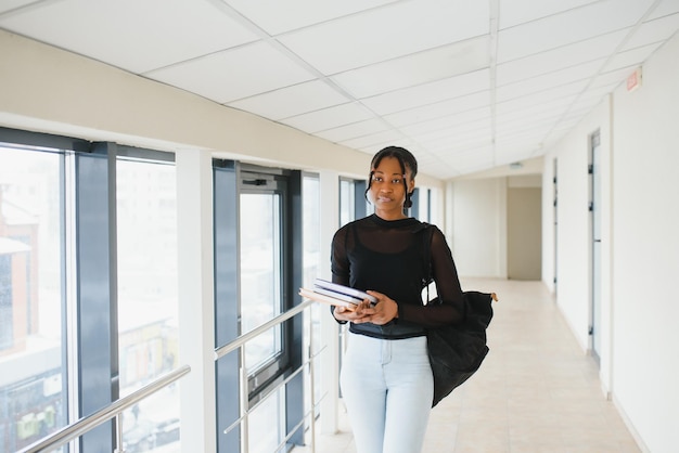 Istruzione liceo apprendimento universitario e concetto di persone sorridente ragazza studentessa afroamericana libro di lettura seduto sulle scale in biblioteca