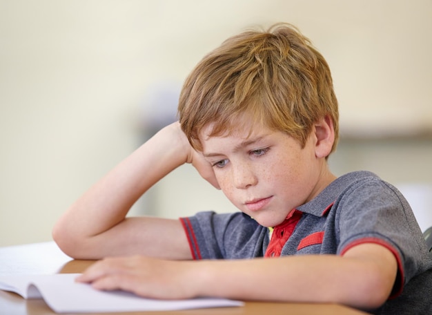 Istruzione scolastica e un ragazzo che legge un libro alla sua scrivania in un'aula per lo studio o lo sviluppo del bambino I bambini imparano e si annoiano con un giovane studente maschio in classe per studiare per un esame o un test