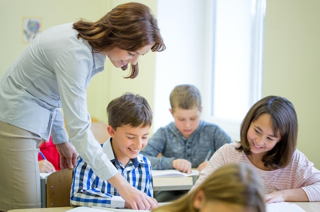 istruzione, scuola elementare, apprendimento e concetto di persone - insegnante che aiuta i bambini delle scuole a scrivere il test in classe