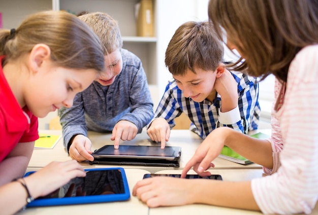 istruzione, scuola elementare, apprendimento, tecnologia e concetto di persone - gruppo di bambini in età scolare con computer tablet pc che si divertono in pausa in classe