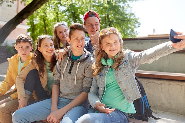 istruzione, scuola superiore, tecnologia e concetto di persone - gruppo di studenti o amici adolescenti felici che prendono selfie con lo smartphone