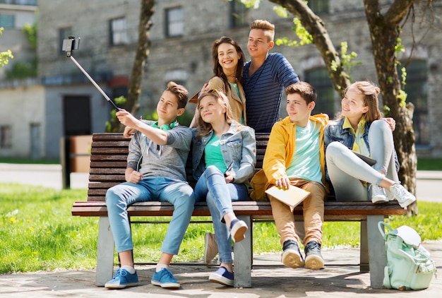 istruzione, scuola superiore, tecnologia e concetto di persone - gruppo di studenti o amici adolescenti felici che prendono selfie con smartphone e monopiede