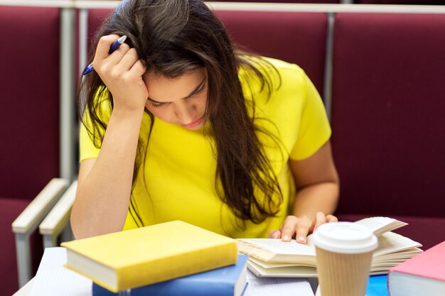 istruzione, scuola superiore, università, apprendimento e concetto di persone - studentessa annoiata con libro di lettura del caffè durante la conferenza