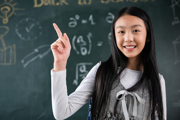 Istruzione Torna al concetto di scuola. Studentessa asiatica in uniforme con zaino in classe che punta il dito sulla lavagna, il bambino delle elementari è in piedi davanti alla classe a scuola pensando a grandi idee