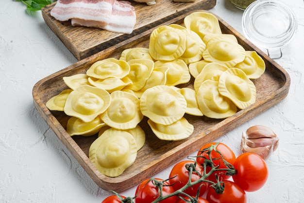 Italiano Ravioli fatti in casa con ingredienti prosciutto basilico pesto mozzarella su vassoio di legno su sfondo bianco