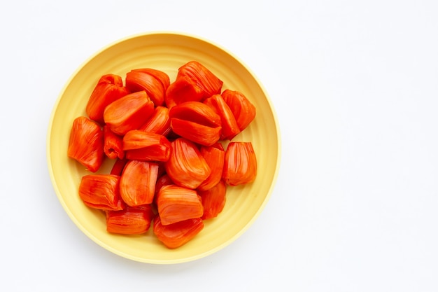 Jackfruit rosso maturo in piatto giallo su fondo bianco.