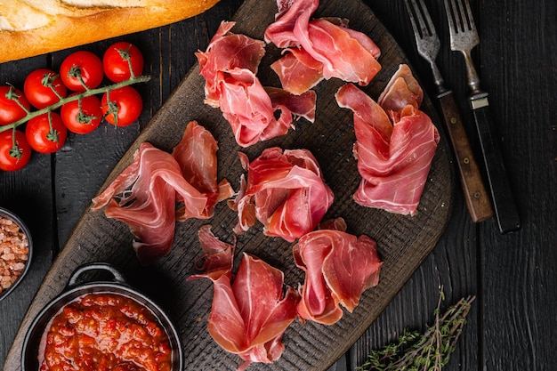 Jamon spagnolo di carne fredda su fondo di legno nero vista dall'alto piatto