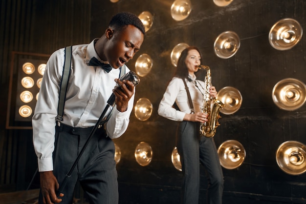 Jazzman maschio e sassofonista femmina con sassofono sul palco con faretti. Artisti jazz che suonano sulla scena