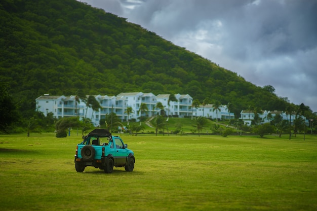 Jeep verde sul campo di erba verde con case bianche e di montagna sullo sfondo con cielo blu.
