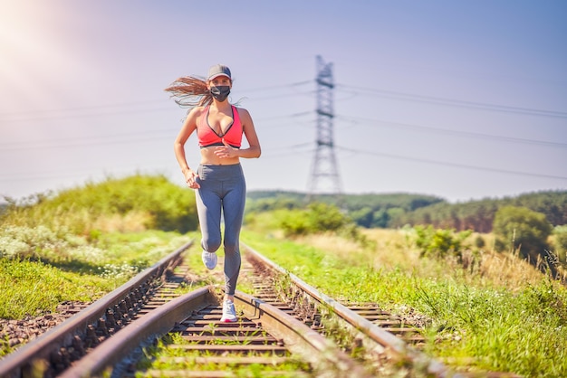 jogger femminile che corre in campagna e indossa una maschera a causa della pandemia di coronavirus