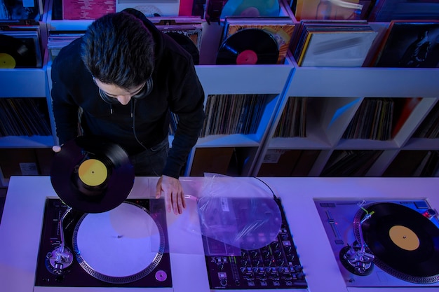 Joven dj mezclando musica en una tienda de discos de vinilo usando un tornamesa de audio