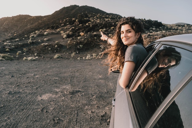 Joven mujer ammirando un paisaje vulcanico asombroso desde su coche al atardecer