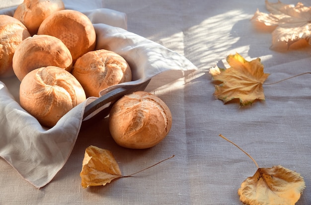 Kaiser, o Vienna panini nel cestino del pane su sfondo tessile con foglie di autunno giallo.