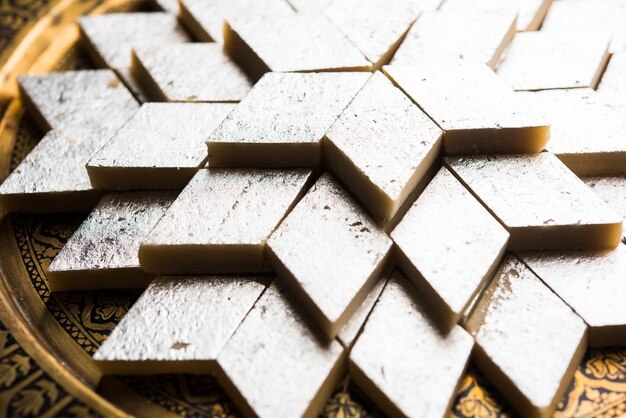 Kaju Katli è un dolce indiano a forma di diamante realizzato con zucchero di anacardi e mava, servito in un piatto su una superficie lunatica. messa a fuoco selettiva