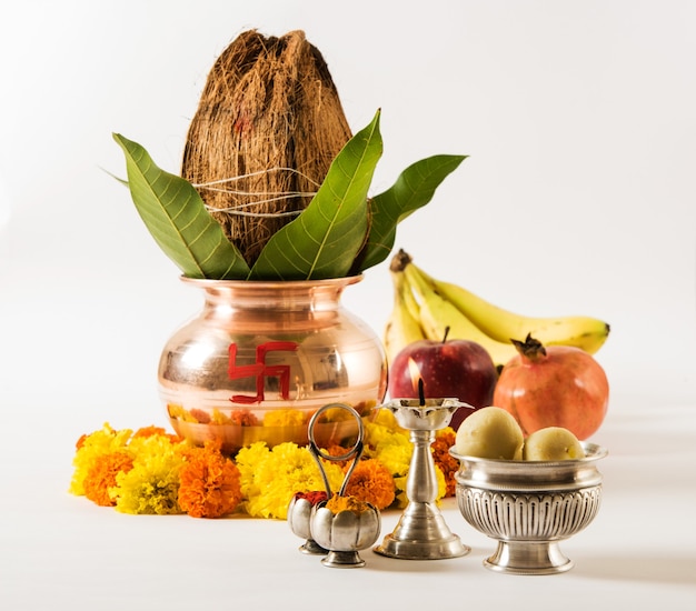 Kalash di rame con cocco e foglia di mango con decorazione floreale, diya, haldi kumkum e dolce pedha,essenziale nella puja indù, vista frontale, primo piano su superficie rossa