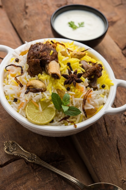 Kashmir Montone Gosht o Agnello Biryani preparato con riso basmati servito con salsa di yogurt su sfondo lunatico, messa a fuoco selettiva