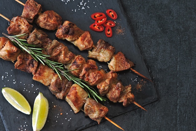 Kebab appetitoso con spezie, peperoncino e lime. Spiedini di maiale profumati su una tavola di pietra.