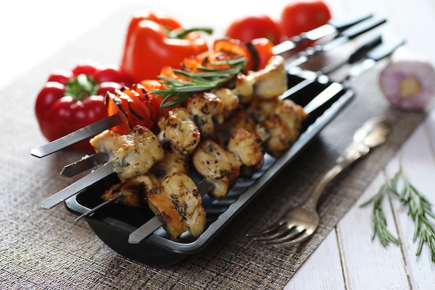 Kebab cotto su spiedini di metallo con verdure servite su tavola bianca