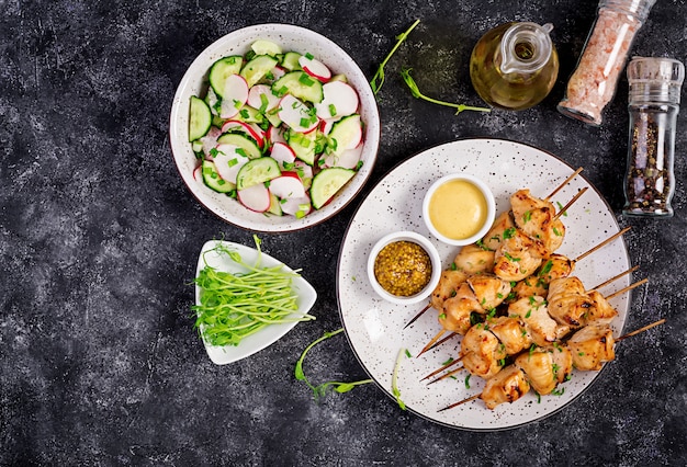 Kebab di pollo alla griglia e insalata con cetriolo, ravanello, cipolla su oscurità.