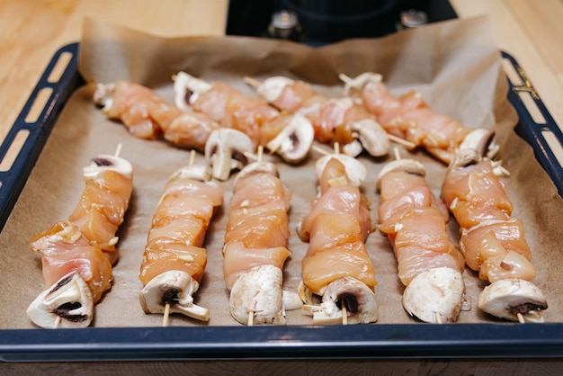 kebab di pollo crudo con champignons su spiedini di legno su carta da forno su vassoio forno pollame marinato