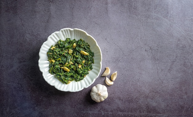 keto diet food spinaci curry in una ciotola bianca con aglio su piastrelle di ardesia nera vista dall'alto