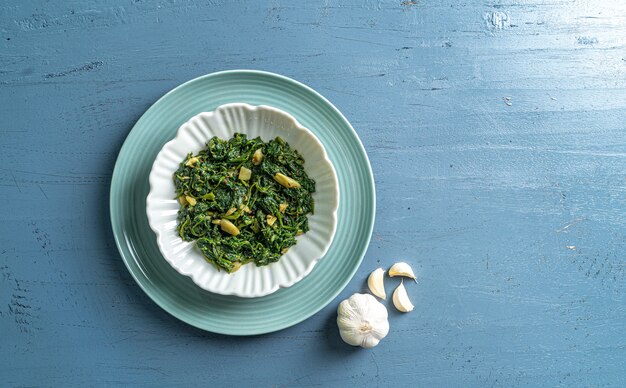 Keto dieta alimentare spinaci curry in ciotola bianca e piatto blu con aglio su tavolo in legno blu vista dall'alto