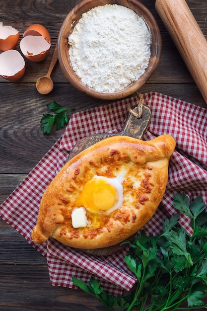 Khachapuri Ajarian fatto in casa fresco su fondo di legno rustico. Barchette di pasta ripiene di formaggio sulguni e uova.