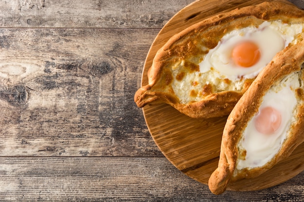 Khachapuri georgiano adiacente tradizionale con formaggio e l'uovo sulla tavola di legno