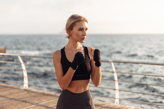 Kickboxer di giovane donna in abbigliamento sportivo con le mani avvolte in bende treni sulla spiaggia all'alba