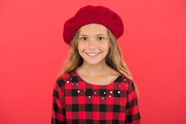 Kid bambina carina sorridente in posa in cappello sfondo rosso. Accessorio berretto alla moda per donna. Come indossare il berretto francese. Ispirazione stile berretto. Come indossare il berretto da fashion girl.