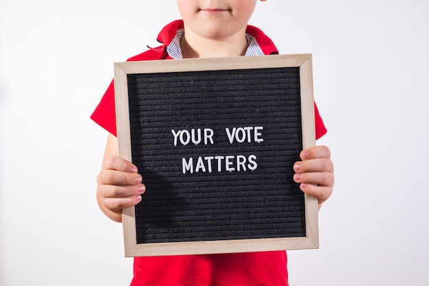 Kid boy holding letter board con testo Your Vote Matters su sfondo bianco