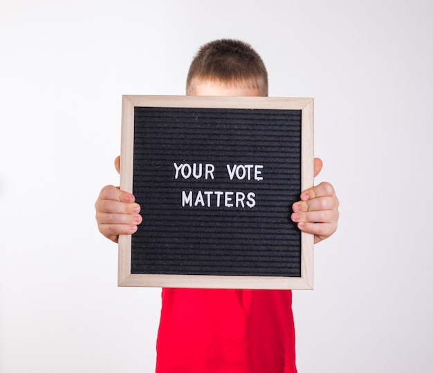Kid boy holding letter board con testo Your Vote Matters su sfondo bianco