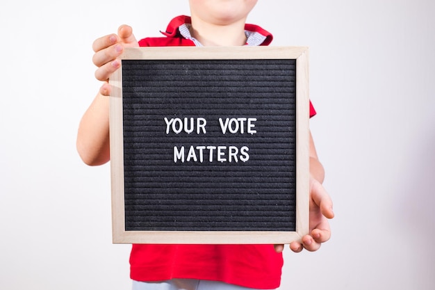 Kid boy holding letter board con testo Your Vote Matters su sfondo bianco