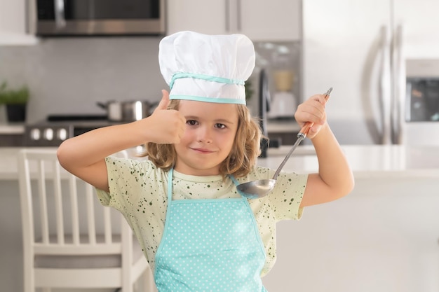 Kid chef cuoco cucina in cucina Ragazzo carino che cucina in cucina a casa cucina Ingredienti sani Ritratto di bambino in uniforme da cuoco Bambino carino per essere uno chef