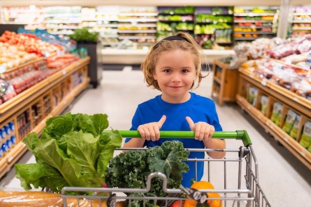 Kid con carrello al supermercato Kid scegliendo frutta e verdura durante lo shopping al supermercato di verdure Ragazzino che va a fare la spesa Cibo sano per i bambini