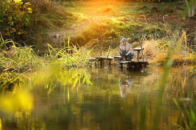 Kid pesca in un fiume seduto su un pontone di legno