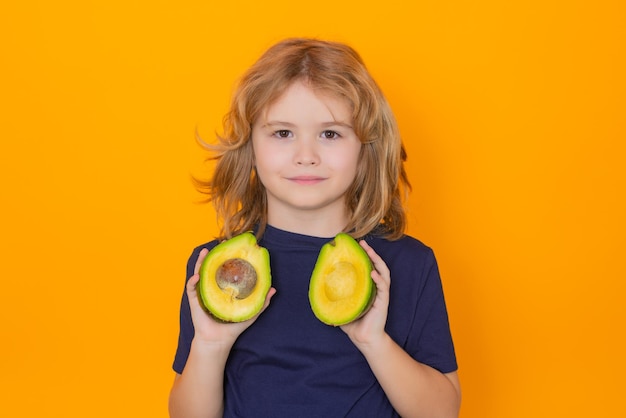 Kid tenere l'avocado rosso in studio Studio ritratto di bambino carino con avocado isolato su sfondo giallo spazio copia