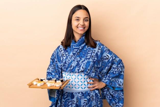 Kimono d'uso della donna e tenere i sushi sopra fondo isolato che posa con le armi all'anca e a sorridere