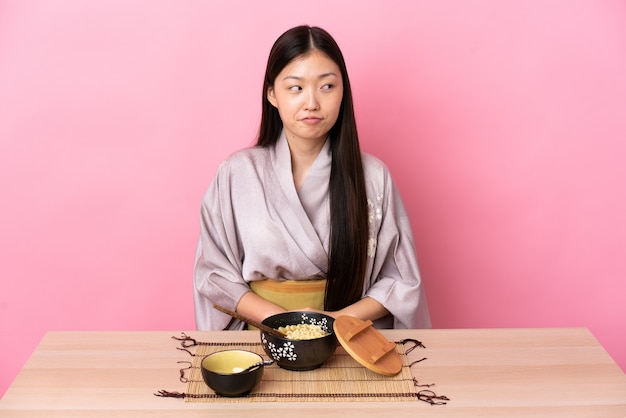 Kimono d'uso della giovane donna cinese e mangiare le tagliatelle che hanno dubbi mentre osservando in su