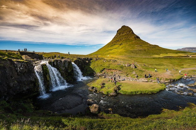 Kirkjufell e Kirkjufellfoss in Islanda con montagna verde, cascata e cielo luminoso in su