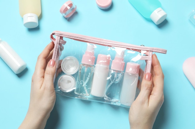 Kit di viaggio cosmetico Donna con borsa di plastica e piccoli contenitori di prodotti per la cura personale su sfondo blu chiaro vista dall'alto