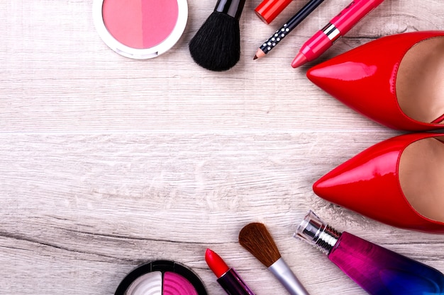 Kit per il trucco e scarpe rosse. Cosmetici su fondo di legno. Un inizio di giornata colorato. La bellezza salverà il mondo.