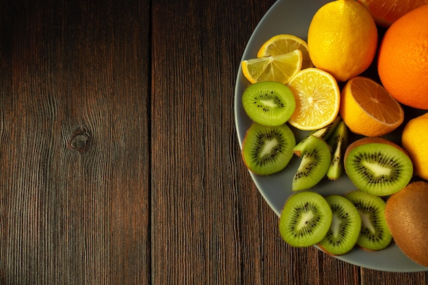 Kiwi, arance e limoni su un piatto su un tavolo di legno scuro