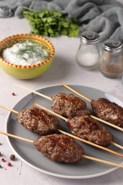 Kofta kebab su spiedini di legno su un piatto e salsa sul tavolo