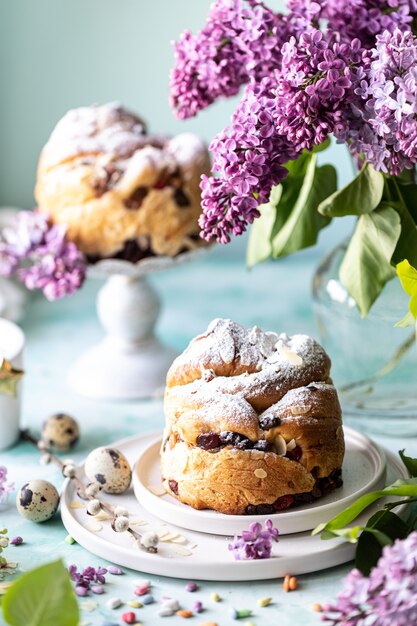 Kraffin tradizionale del dolce di Pasqua del bigné con l'uva passa e lo zucchero a velo sulla tavola. Torte pasquali, candele e un mazzo di fiori lilla.