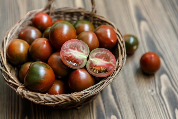 Kumato - varietà scura di pomodoro - in una ciotola fatta a mano in salice intrecciato sullo sfondo di legno scuro