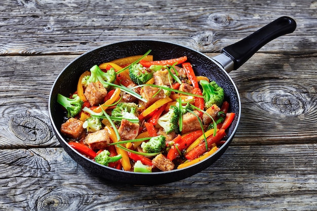 Kung pao tofu con peperoni misti, broccoli e scalogno in padella su un tavolo in legno rustico, cucina cinese, vista del paesaggio dall'alto